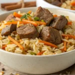 A bowl filled with beef plov, featuring tender chunks of beef, fluffy long-grain rice, and julienned carrots, garnished with fresh herbs.
