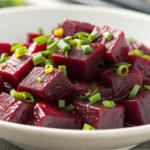 Close-up of a Russian beet salad with vibrant beet cubes garnished with freshly chopped green onions, served in a white bowl.
